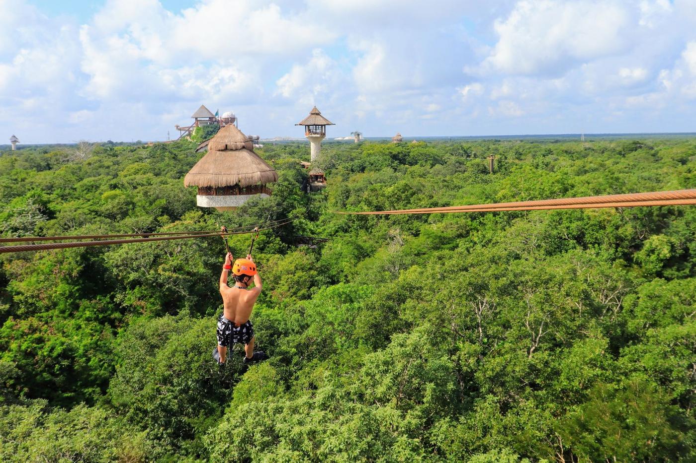 Visiteur en tyrolienne au-dessus de la canopée du parc Xplor, les tours du parcours à l'horizon, Quintana Roo, Mexique